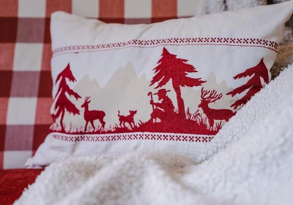 Red and white cushion decorated with a shepherd, a dog, trees and deer