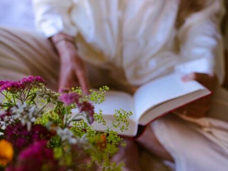 Eine Ältere Dame liest ein Buch neben einem Blumenstrauch