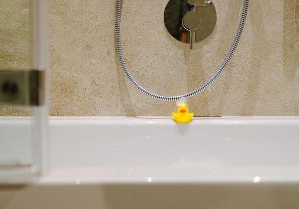 A bath duck at the edge of the bathtub with foam in the face