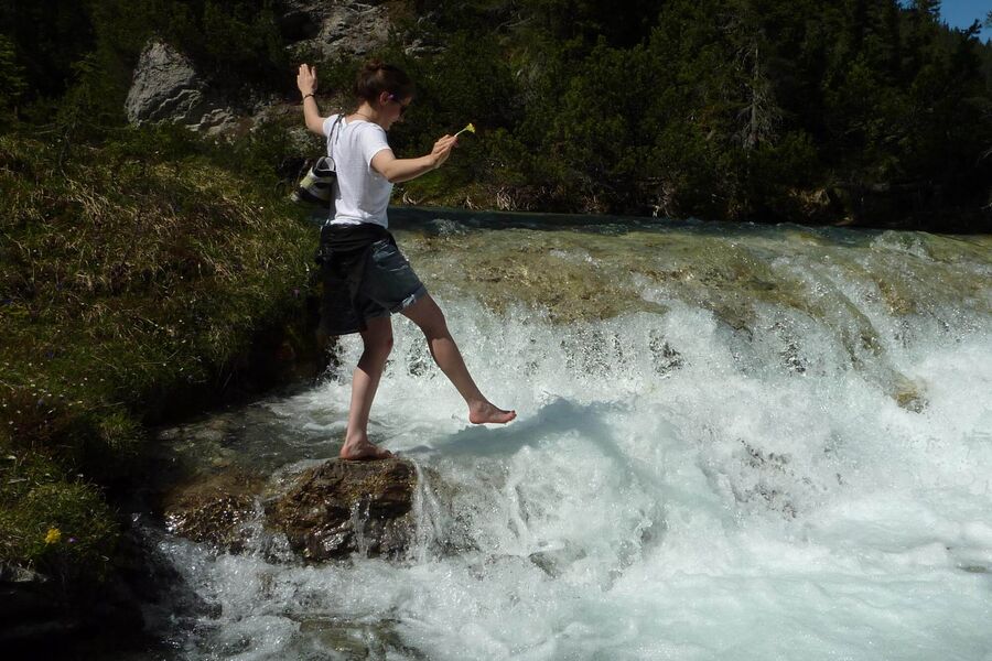 Eine junge Frau genießt das eiskalte Schmelzwasser, das in diversen Bächen die Alpen hinabstürzt