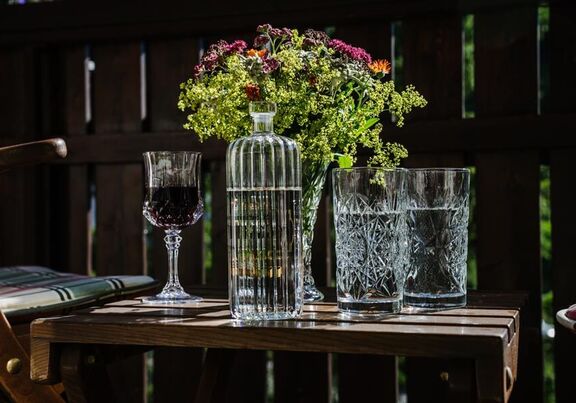 Wasserkaraffe, zwei Gläser mit Wasser, ein Weinglas und ein Blumenstrauß auf einem Holztisch