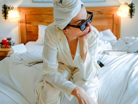 A woman sits on the bed and looks thoughtfully out of the window.