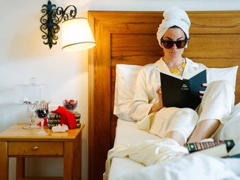 Woman in swimsuit and sunglasses reading a book in bed