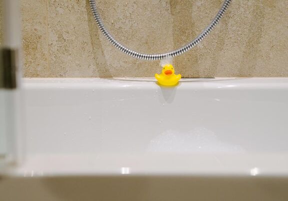 A bath duck at the edge of the bathtub with foam in the face