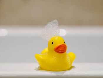 Eine Quietscheente am Badewannenrand mit einer Schaumkrone