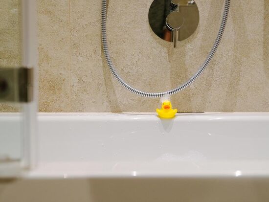 A bath duck at the edge of the bathtub with foam in the face