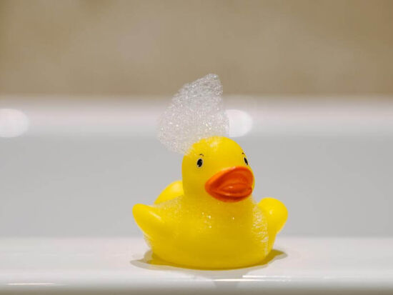 Eine Quietscheente am Badewannenrand mit einer Schaumkrone