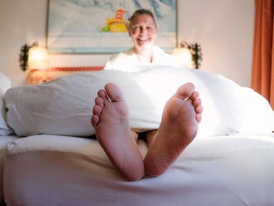 Eine Frau sitzt im Bett und lässt ihre Füße am Bettrand baumeln.