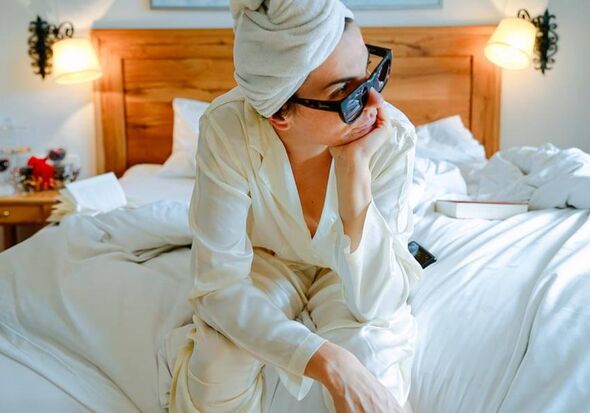 A woman sits on the bed and looks thoughtfully out of the window.