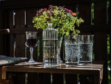 Wasserkaraffe, zwei Gläser mit Wasser, ein Weinglas und ein Blumenstrauß auf einem Holztisch