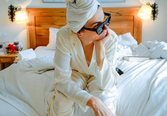 A woman sits on the bed and looks thoughtfully out of the window.