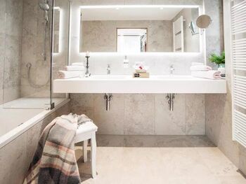 Ein weißes Badezimmer mit Badewanne, zwei Waschbecken und einen Kleien Sessel