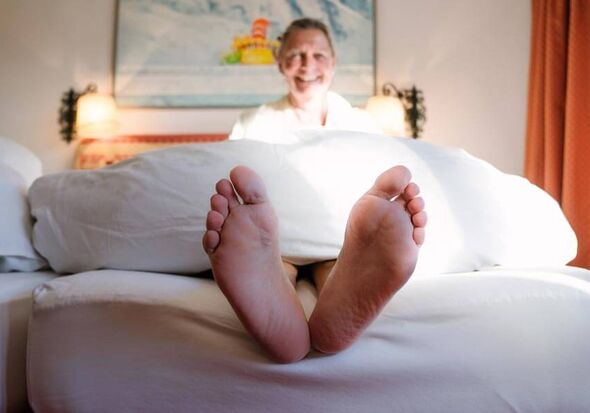 Eine Frau sitzt im Bett und lässt ihre Füße am Bettrand baumeln.