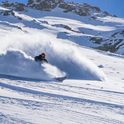 A person skis and swirls up a lot of snow
