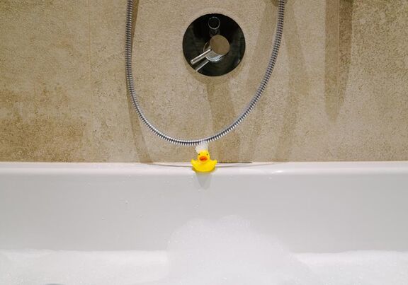 Eine Badente am Badewannen Rand mit Schaum im Gesicht