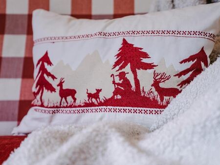 Red and white cushion decorated with a shepherd, a dog, trees and deer