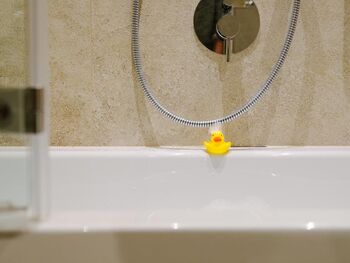A bath duck at the edge of the bathtub with foam in the face
