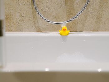 A bath duck at the edge of the bathtub with foam in the face