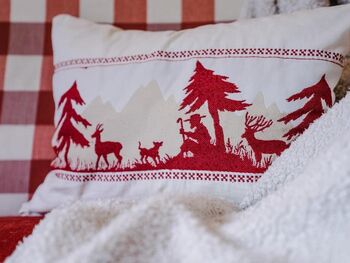 Red and white cushion decorated with a shepherd, a dog, trees and deer
