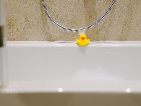 A bath duck at the edge of the bathtub with foam in the face