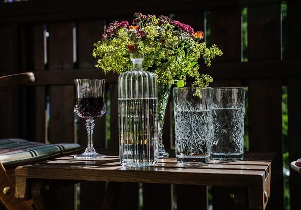 Wasserkaraffe, zwei Gläser mit Wasser, ein Weinglas und ein Blumenstrauß auf einem Holztisch