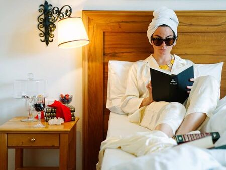 Woman in swimsuit and sunglasses reading a book in bed