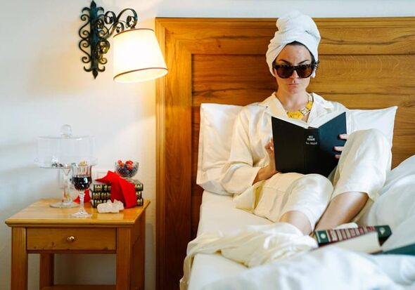 Woman in swimsuit and sunglasses reading a book in bed