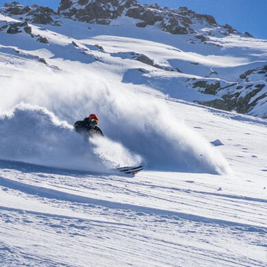 A person skis and swirls up a lot of snow