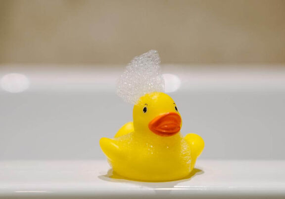 Eine Quietscheente am Badewannenrand mit einer Schaumkrone